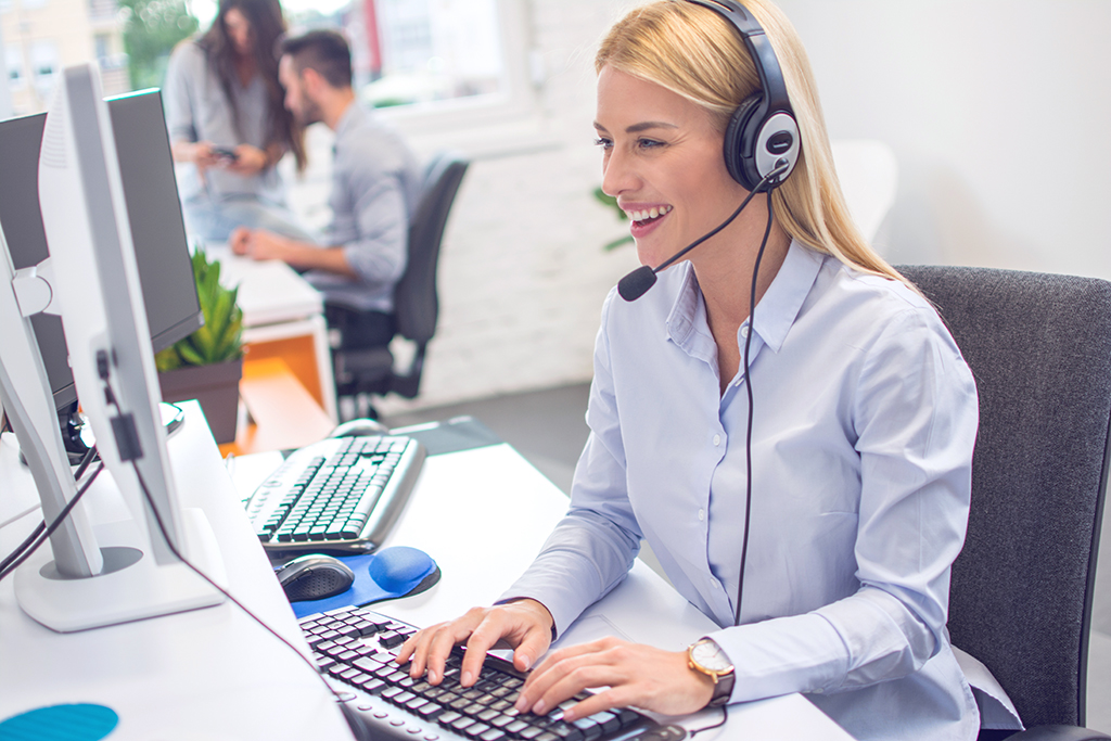 Smiling female helpline operator with headset using computer at office.