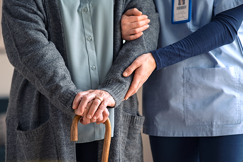 Sairaanhoitaja avustaa senioria jolla on kävelykeppi