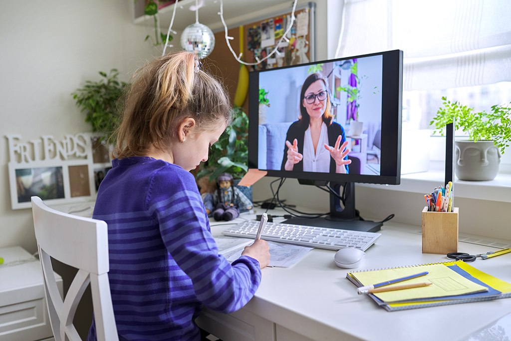 Child girl studying with teacher remotely on computer using video call