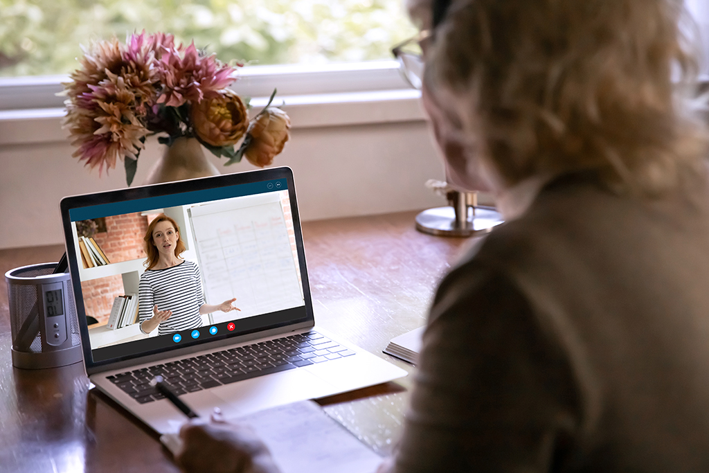 Rear view close up mature woman watching webinar, using laptop